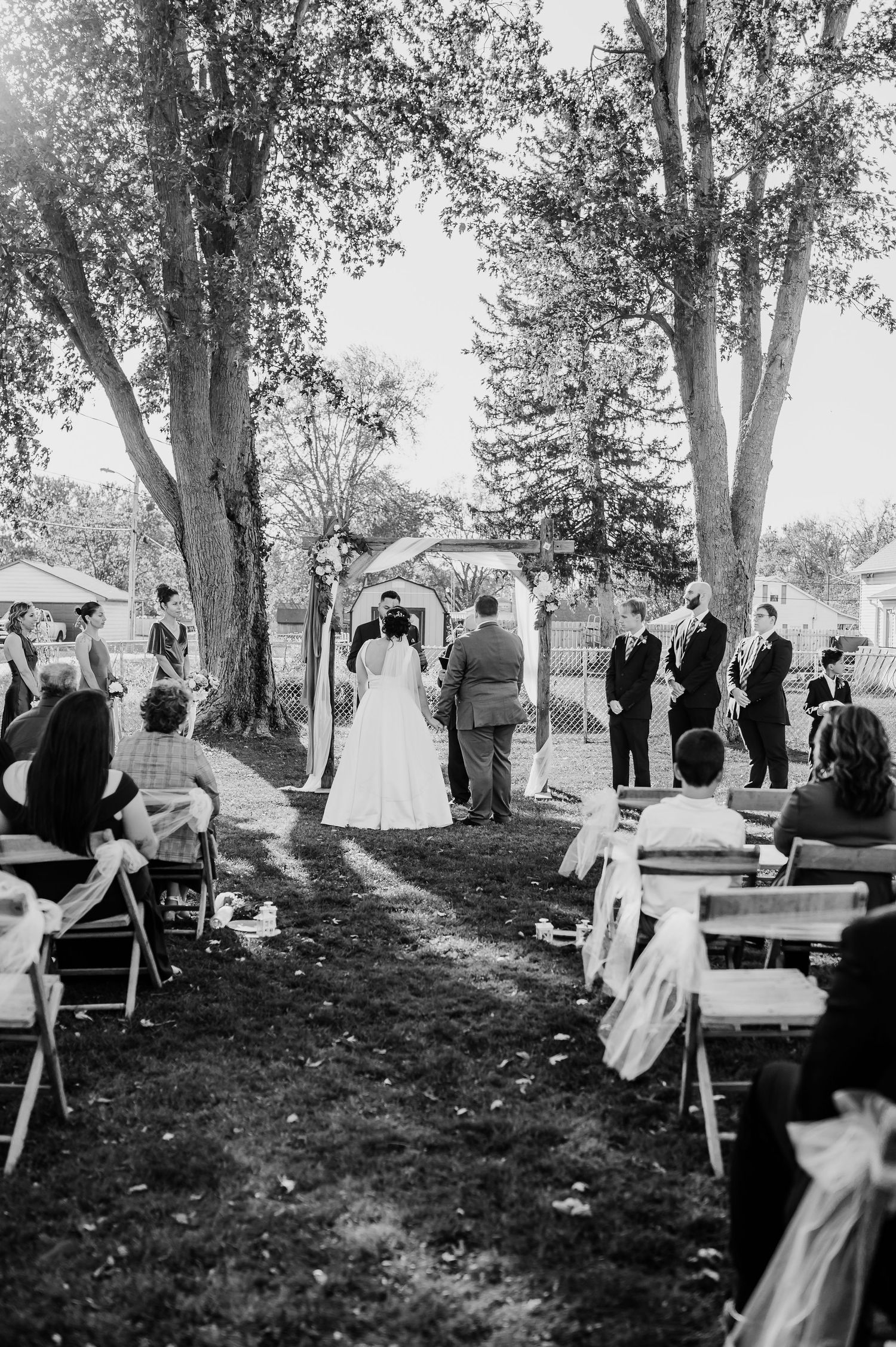 Black and white photo sequence showing a wedding ceremony under tall trees with guests seated outdoors.