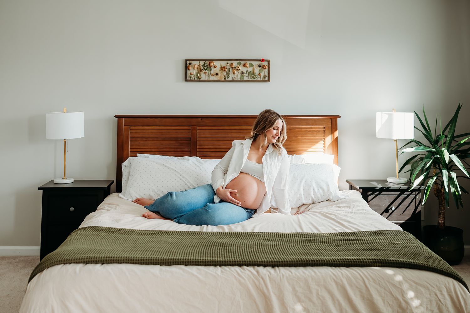 Someone rests on a bed with white linens and olive green throw blanket, flanked by nightstands with table lamps.