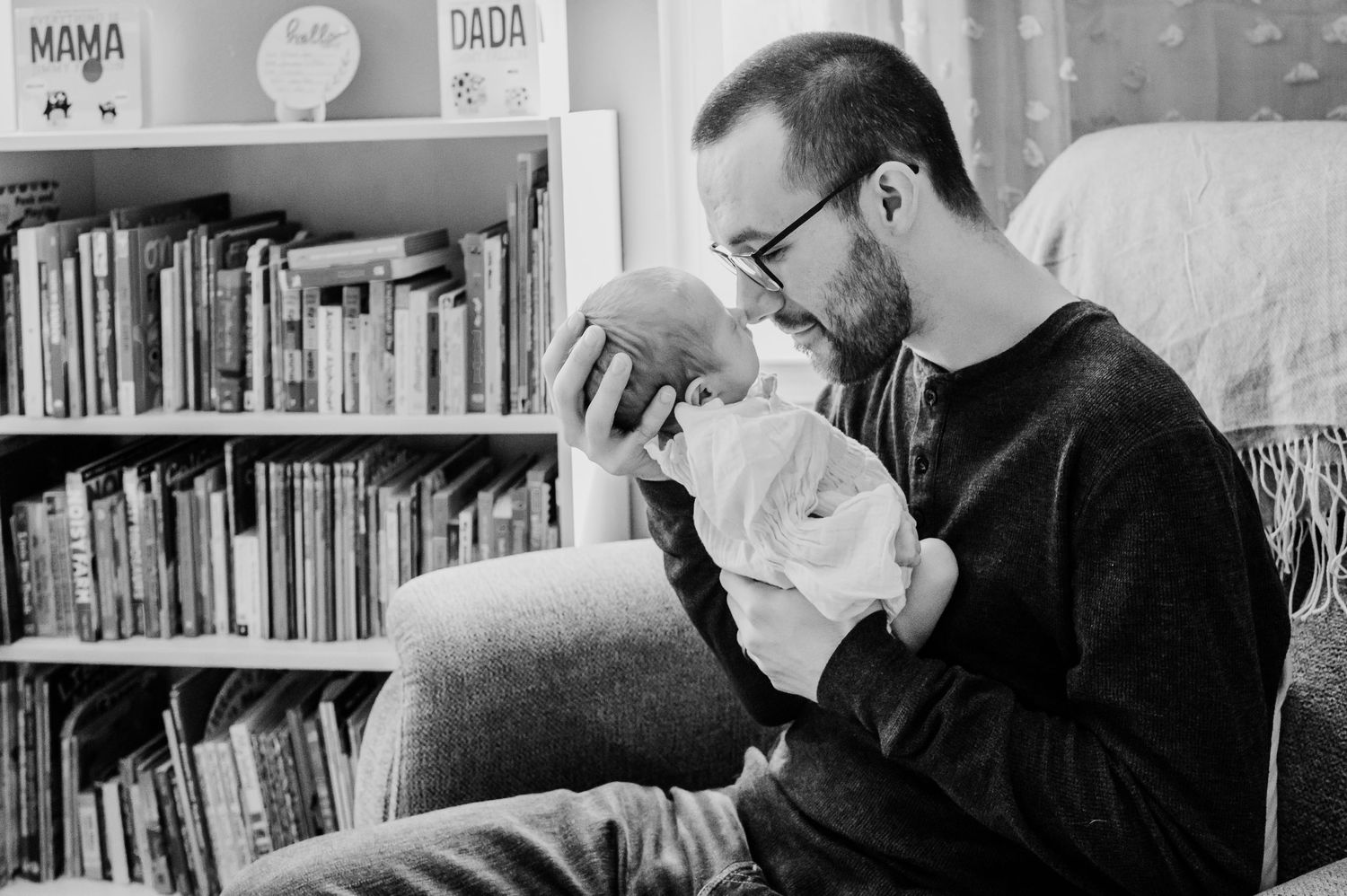 Black and white photo showing a Noblesville, Indiana, dad cuddling with newborn daughter in nursery.