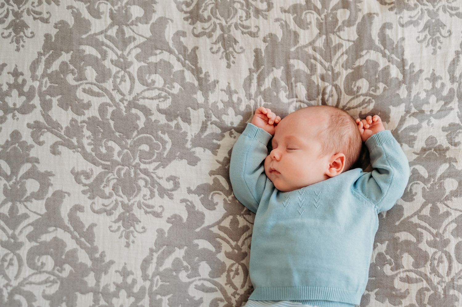 A sleeping baby in a light blue outfit sleeps on a gray and white patterned comforter during Westfield, Indiana, in-home newborn session.