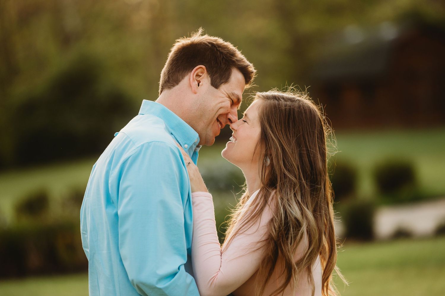 Romantic couple embraces during golden hour spring maternity photoshoot wearing coordinating blue and neutral outfits.