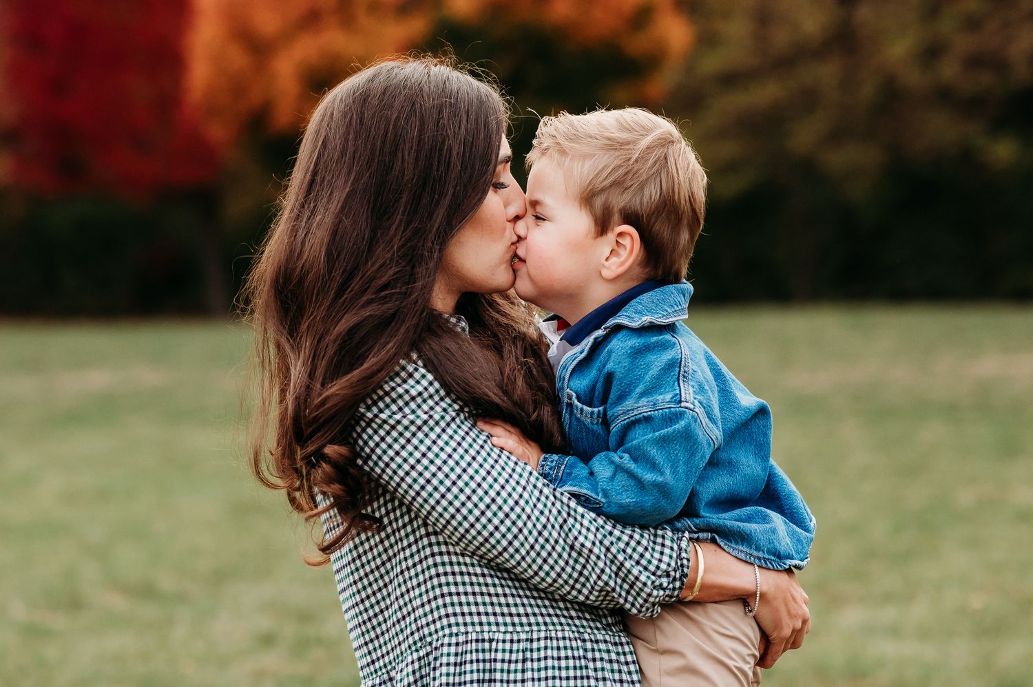 A mother and young child share tender moments together in a grassy outdoor setting during fall family photos in Avon, Indiana.