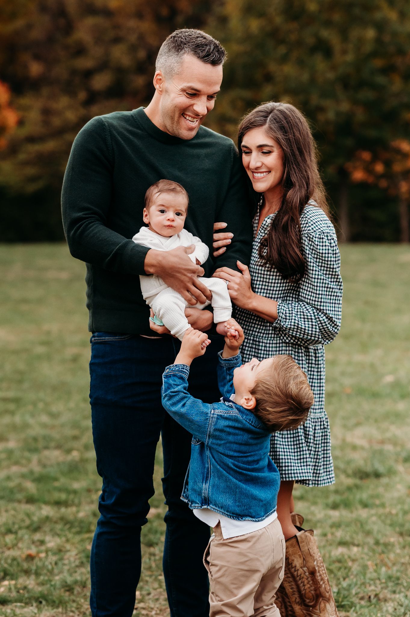 A family shares joyful moments together on a grassy field during an outdoor fall newborn photo session in  Avon, Indiana.