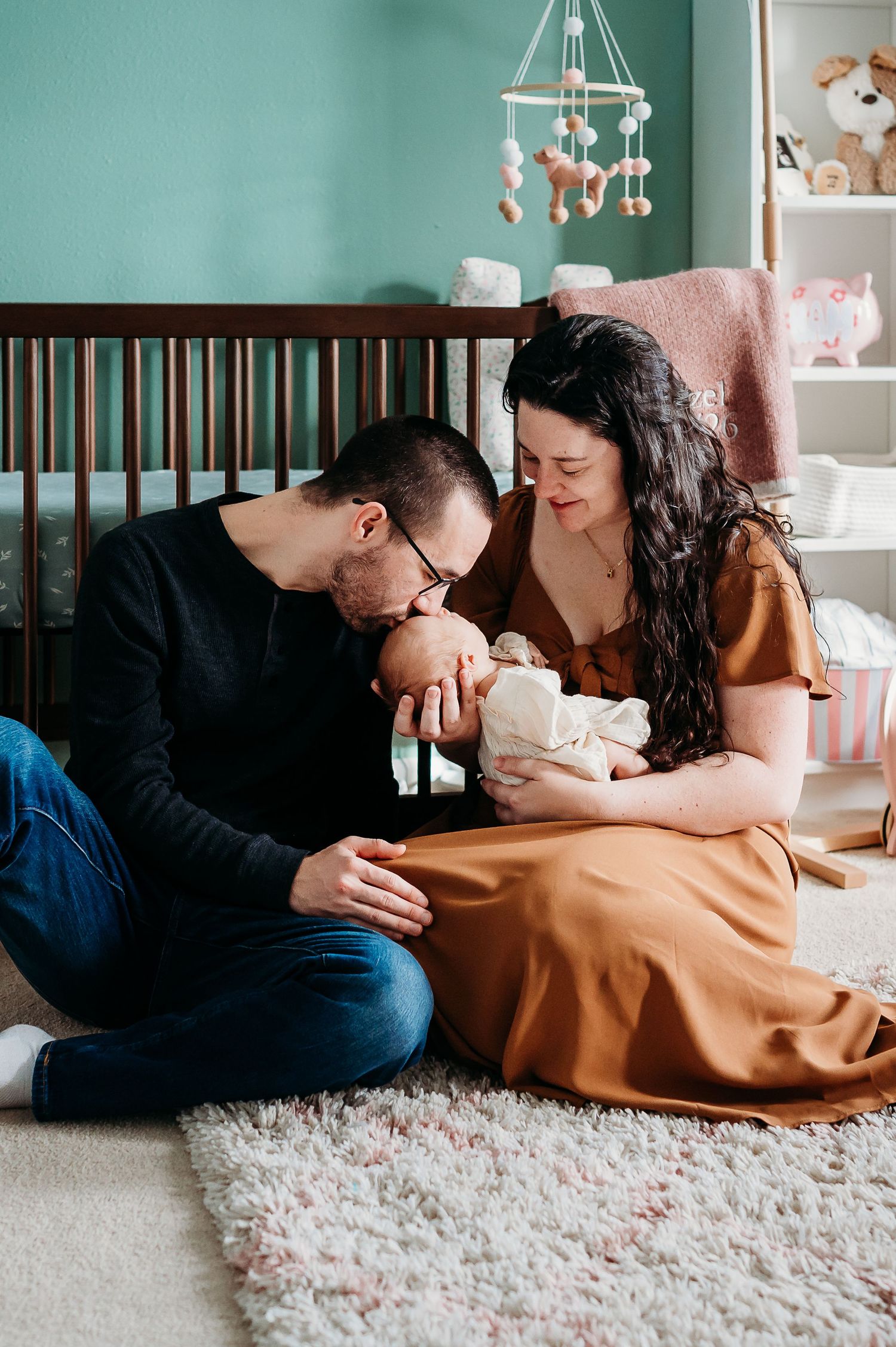 A family shares tender moments while lying on a plush white carpet in a nursery setting.