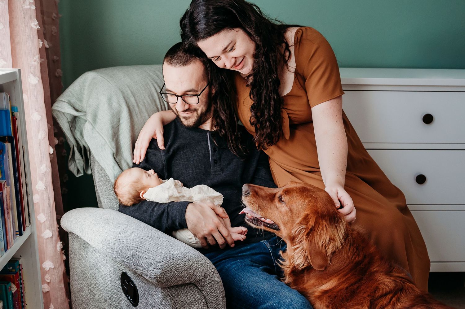 A couple sits together in a cozy corner reading while petting their golden retriever dog.