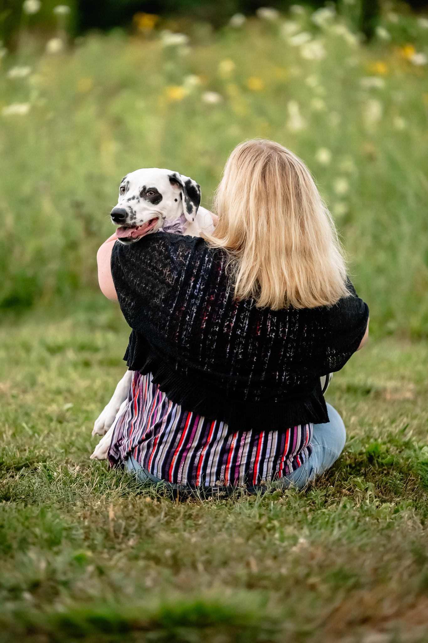Blonde woman sitting on grass hugging a Dalmatian dog in a flower-filled meadow in Danville, Indiana, with Sara House Photography.