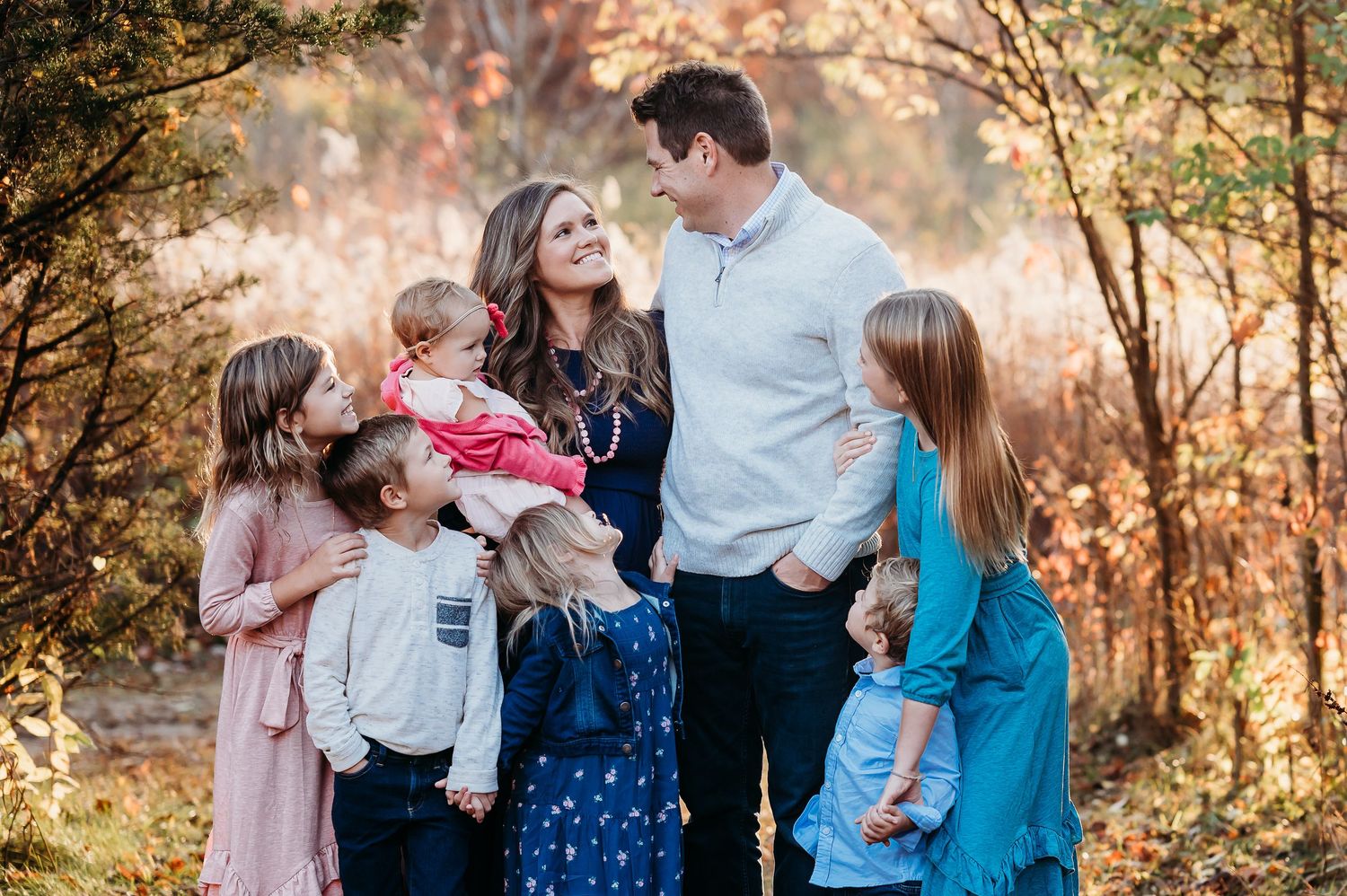 A Fishers, Indiana, family shares tender moments together in a sunlit autumn forest setting during a professional photo session.