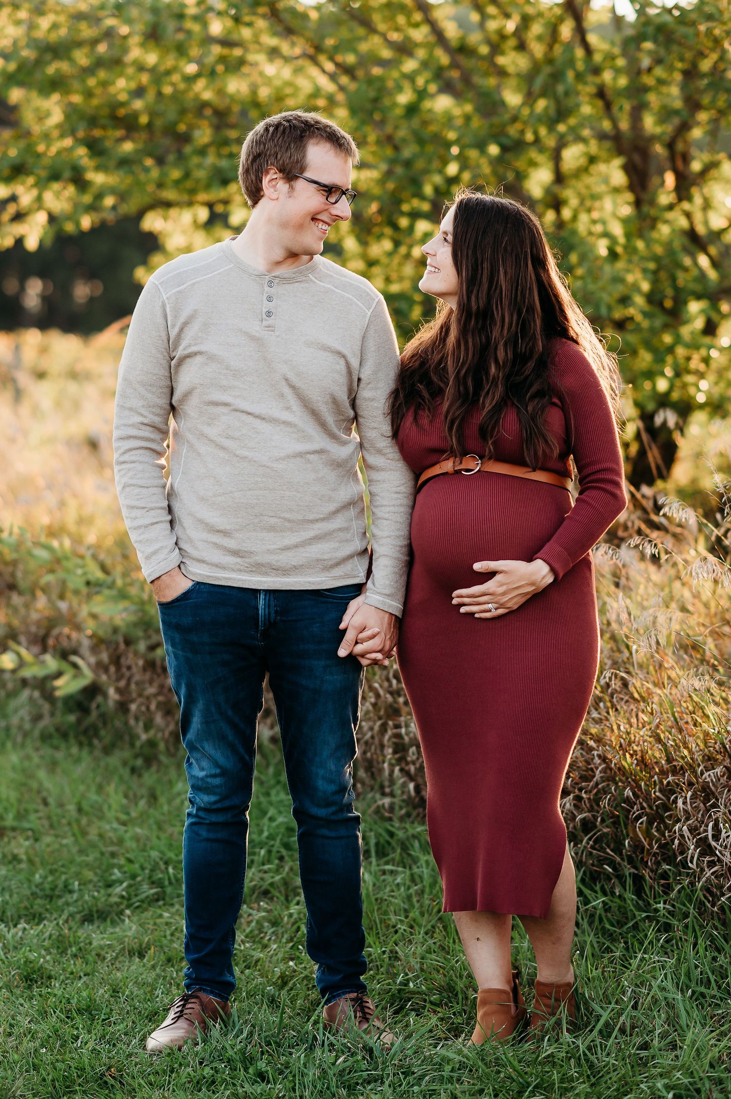A couple in burgundy dress and beige sweater share intimate moments during an outdoor autumn maternity photoshoot in West Lafayette, Indiana