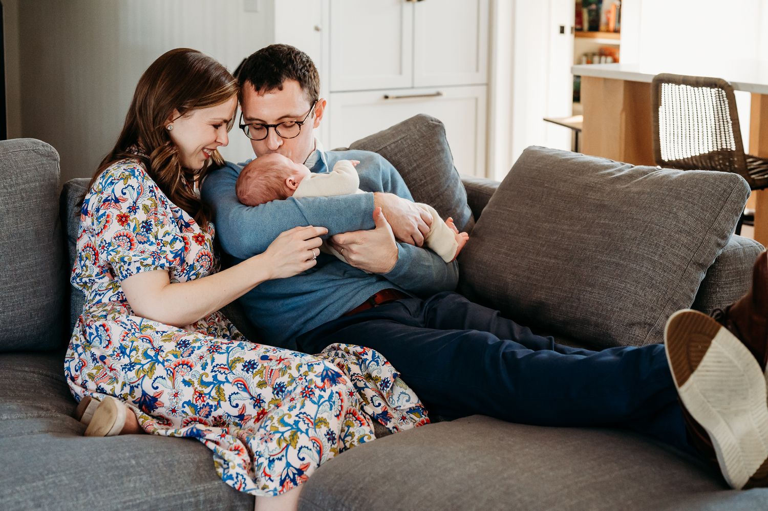 Family cuddling with newborn baby on couch in natural window light at home during Westfield lifestyle newborn session.