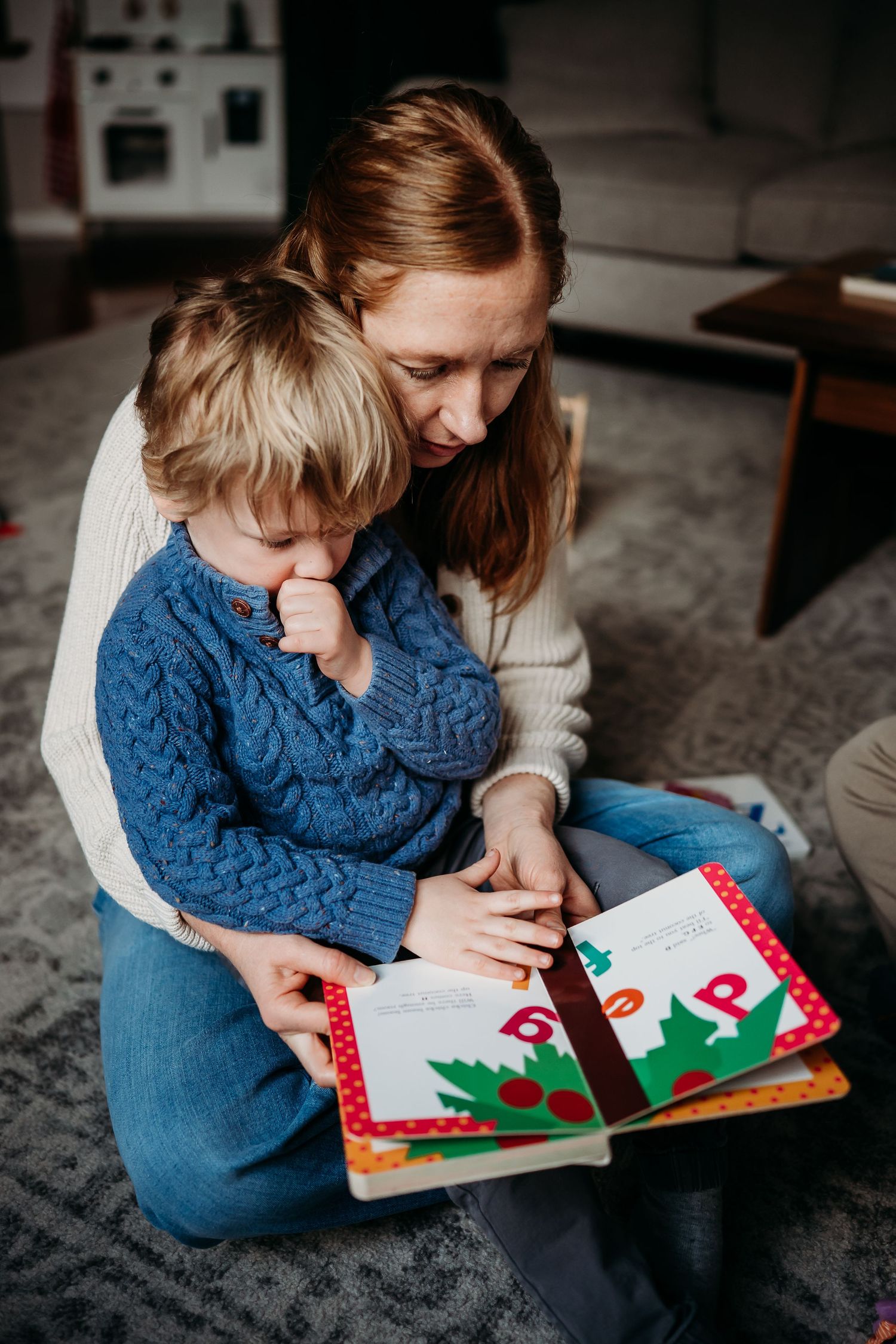 Mother and toddler reading a colorful picture book together on the floor at home.