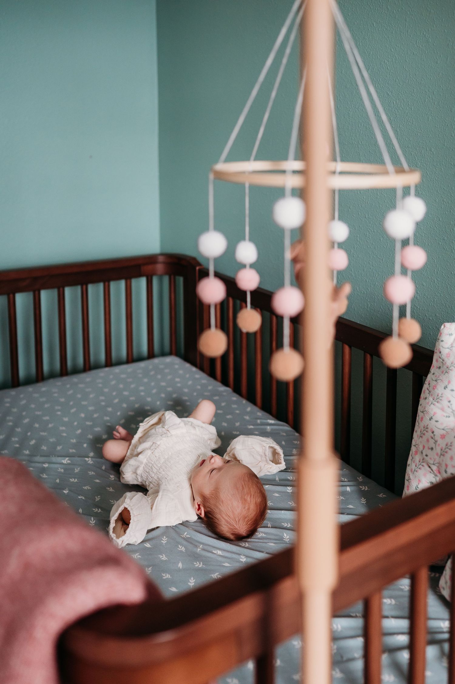 A baby mobile with white hanging spheres hangs above a dark wooden crib with gray polka dot bedding.