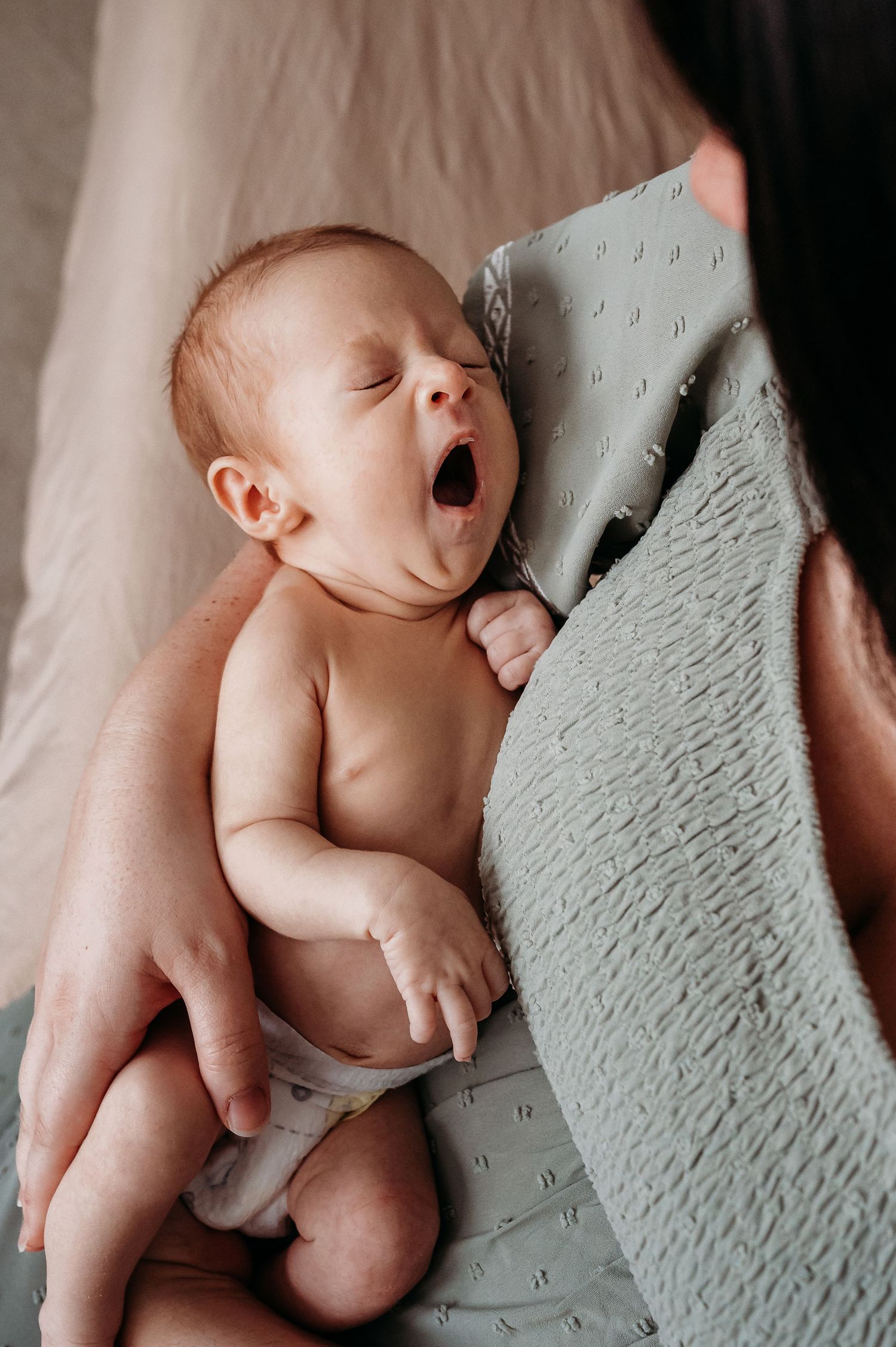 A sleeping newborn baby yawns while resting in Noblesville mother's arms.