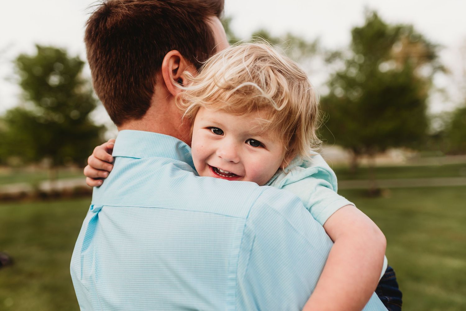 A sweet boy hugs dad during golden hour, wearing coordinating blue outfits.
