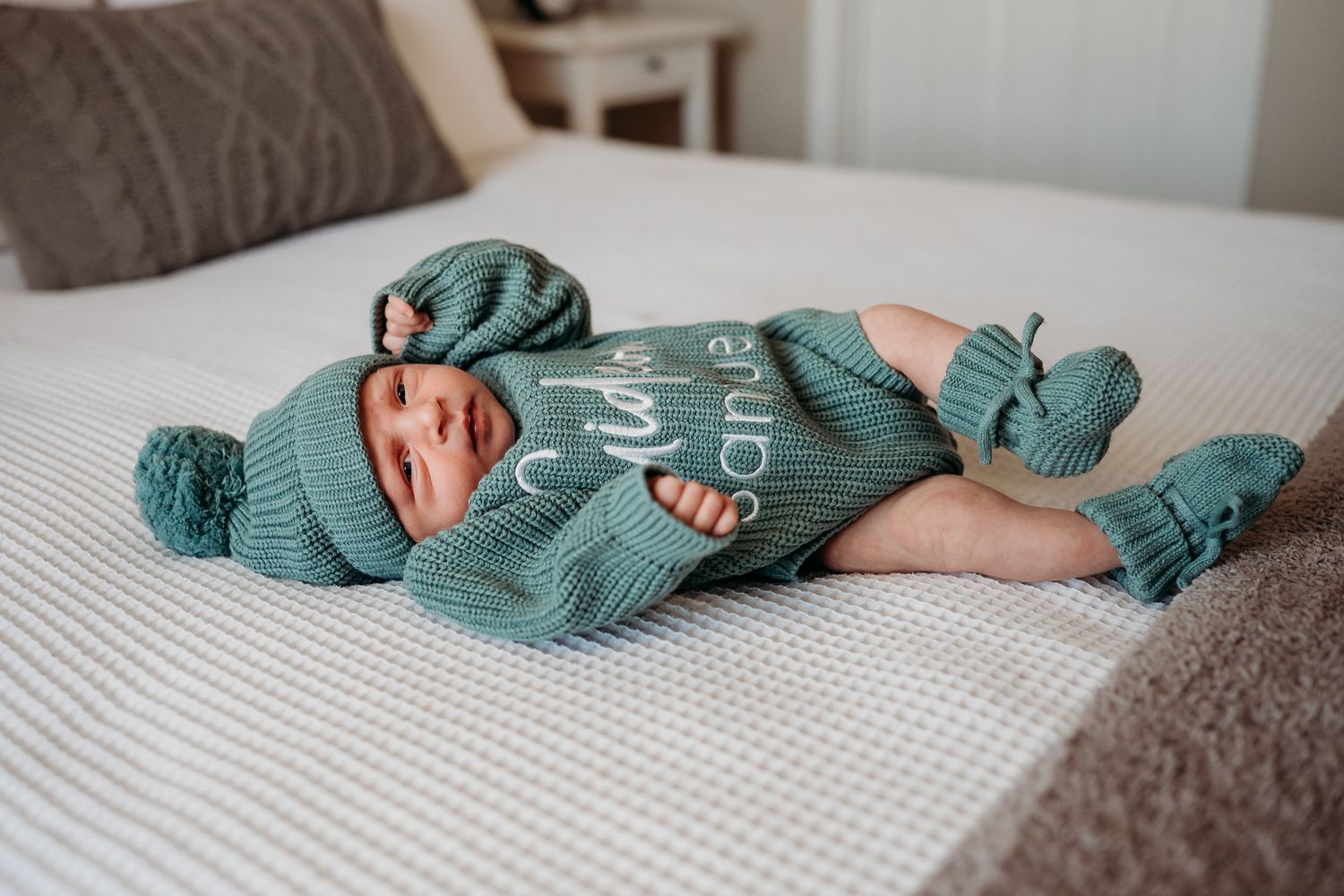Greenwood, Indiana, baby wearing a teal knit outfit laying on white bedding during lifestyle newborn photoshoot with Sara House Photography.