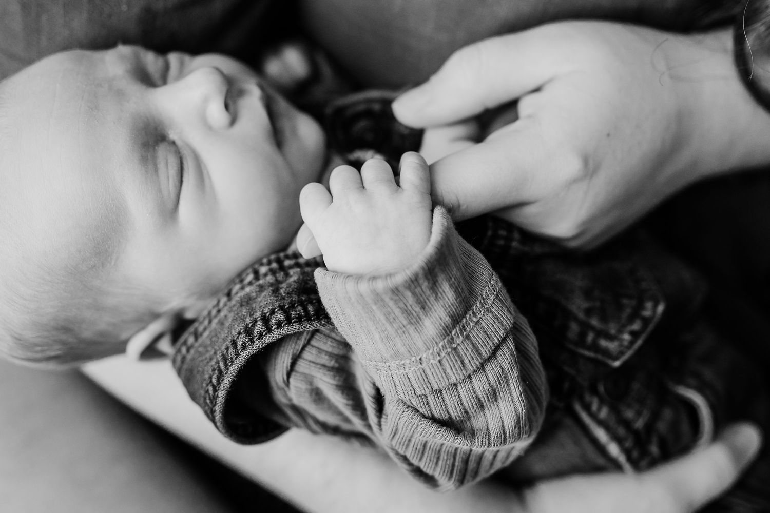 Black and white photo of a sleeping newborn baby gently gripping an adult's finger.