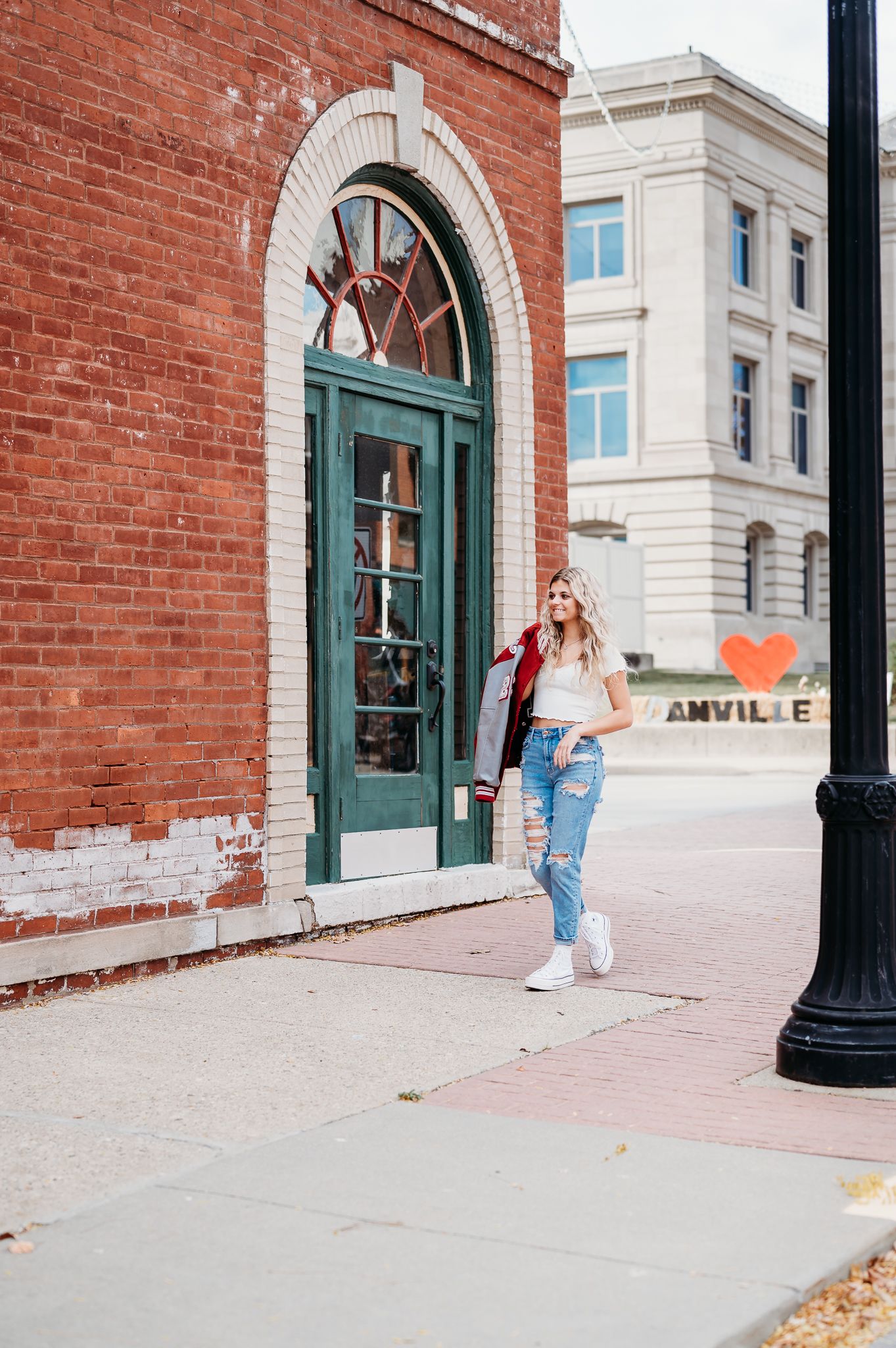 Stylish street scene with brick building facade featuring arched teal doorway and girl posing on sidewalk in casual attire in Danville.