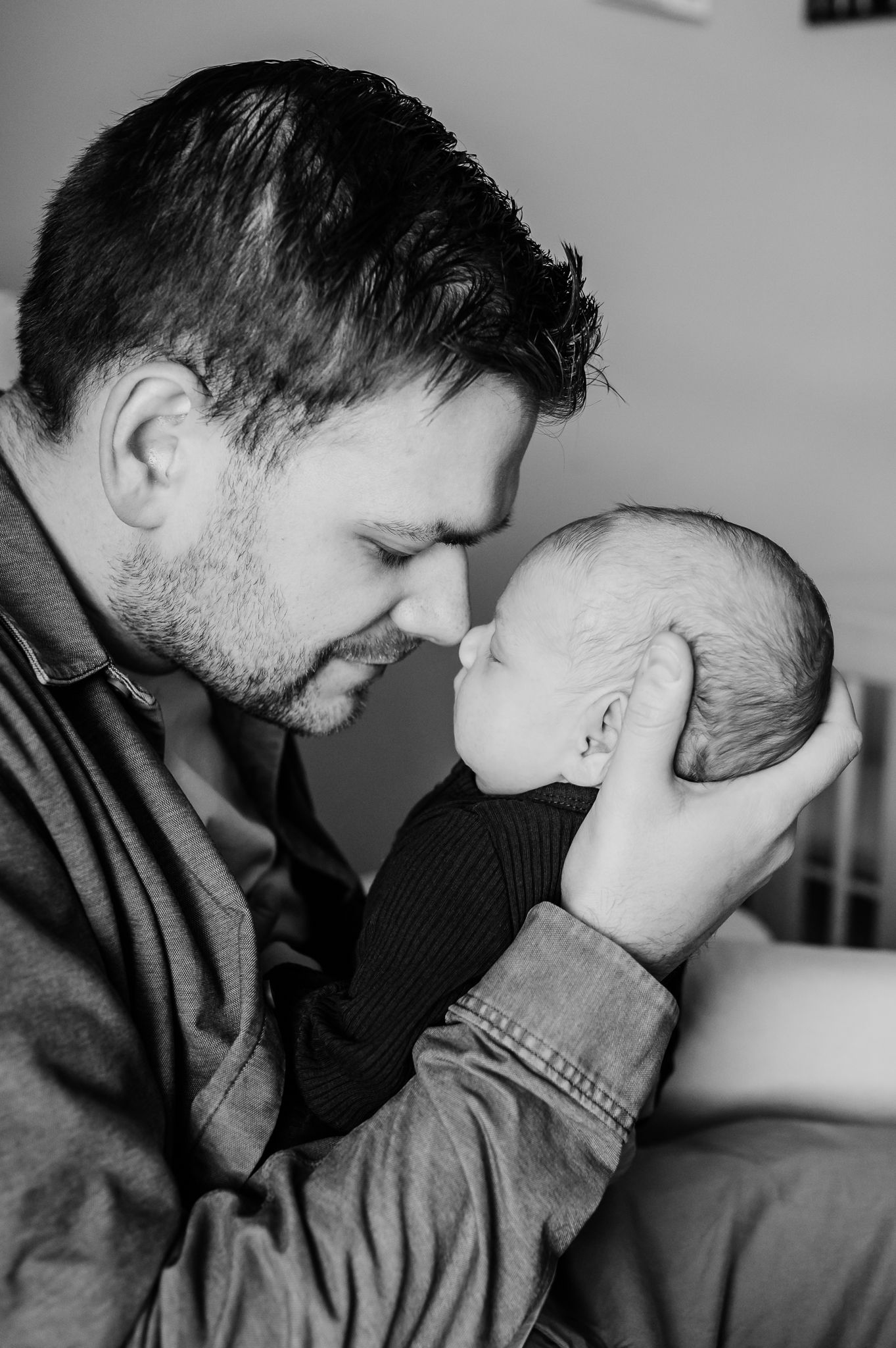 A tender black and white portrait of a dad gently holding and connecting with their newborn baby boy in Carmel, Indiana, home.
