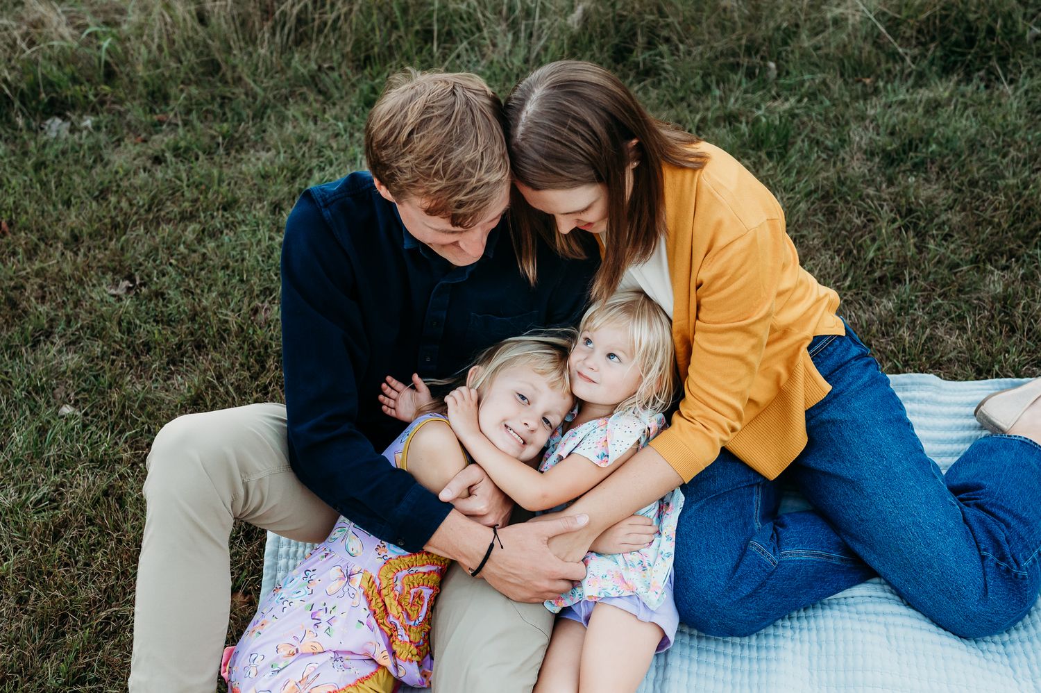 A family sits together on a blanket outdoors, sharing a tender moment while embracing on the grass at Avon's Washington Township Park.