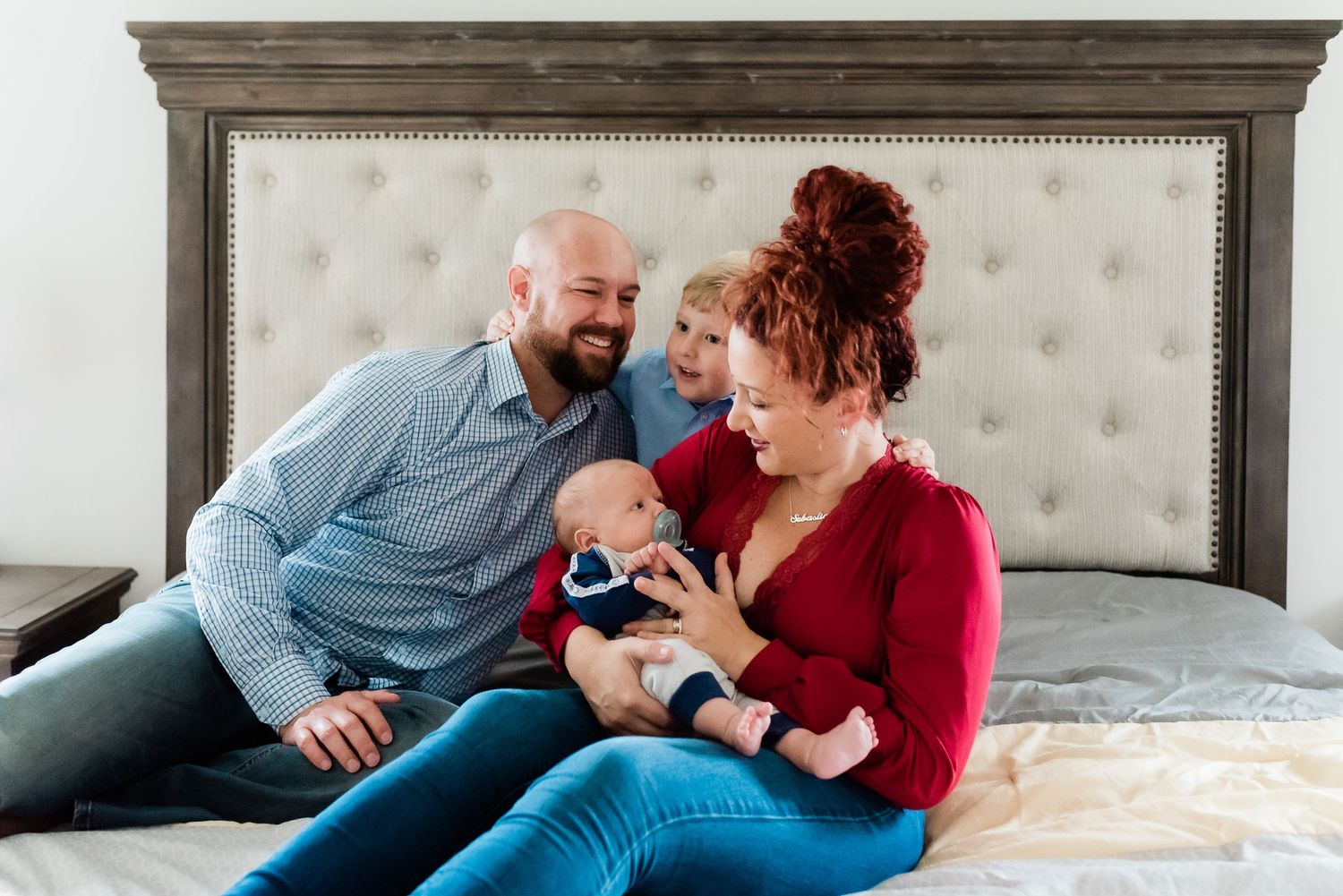 Family snuggles together on a cozy bed during a lifestyle newborn photography session in Avon, Indiana, home.