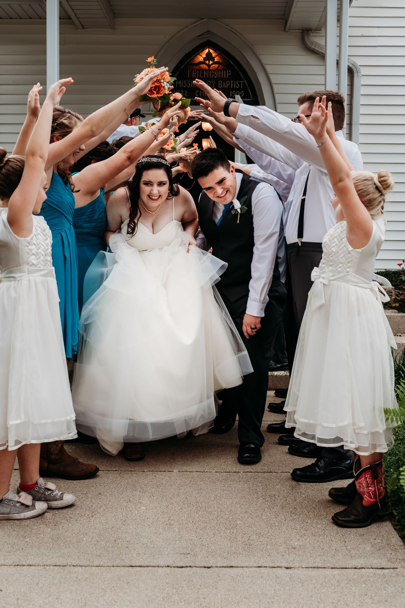 Wedding party members show off their colorful socks in a fun lineup pose outside a white building.