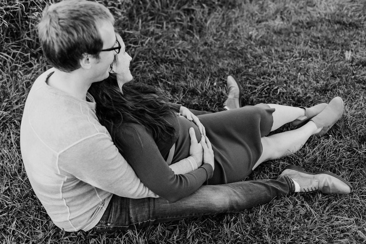 Black and white photo of pregnant mom and husband lying in the grass during outdoor maternity session at Prophetstown State Park in Indiana.