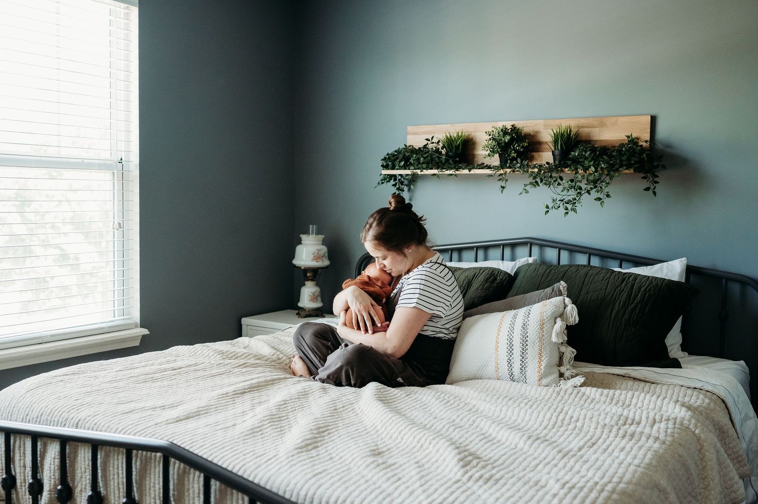 A mom and baby snuggling together in bedroom with dark green walls during photo session with Indianapolis family and newborn photographer.