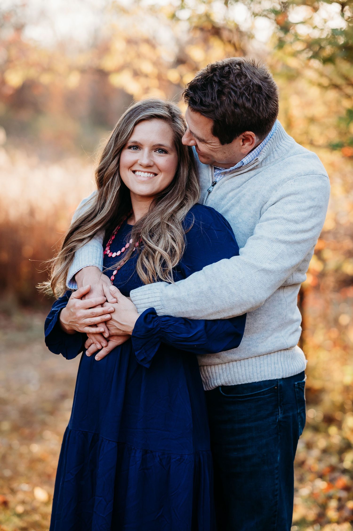 Couple embraces in romantic autumn photoshoot with golden sunlight filtering through fall foliage.