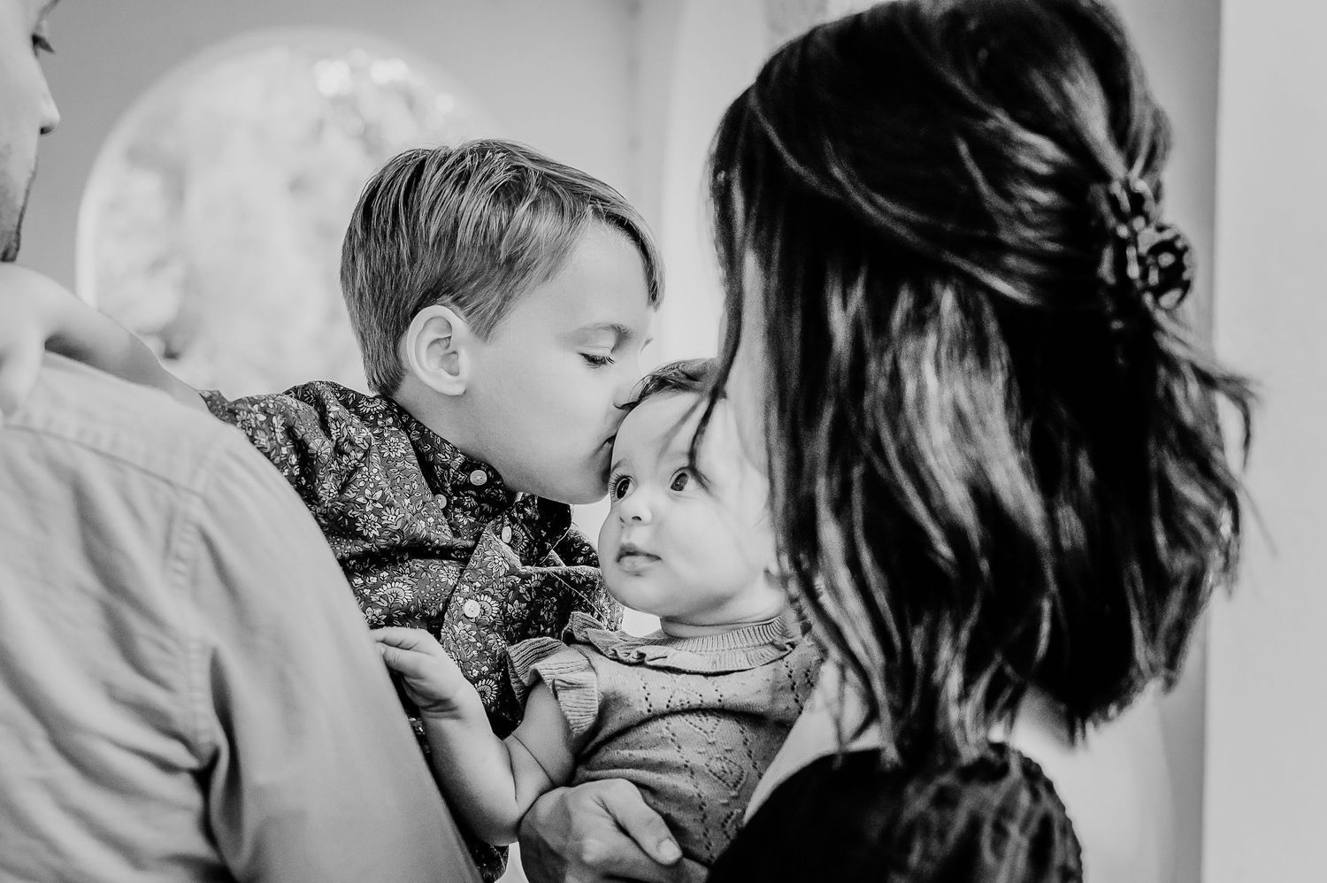 A black and white photograph showing brother kissing baby sister.