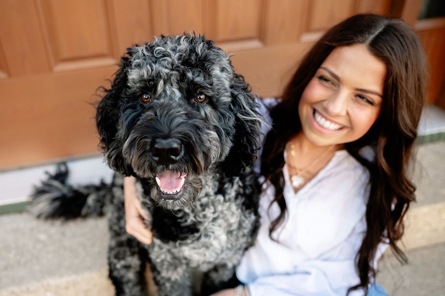 Smiling young woman with long dark hair posing outdoors with a fluffy black Bernedoodle/Labradoodle mix dog near door in Downtown Danville.