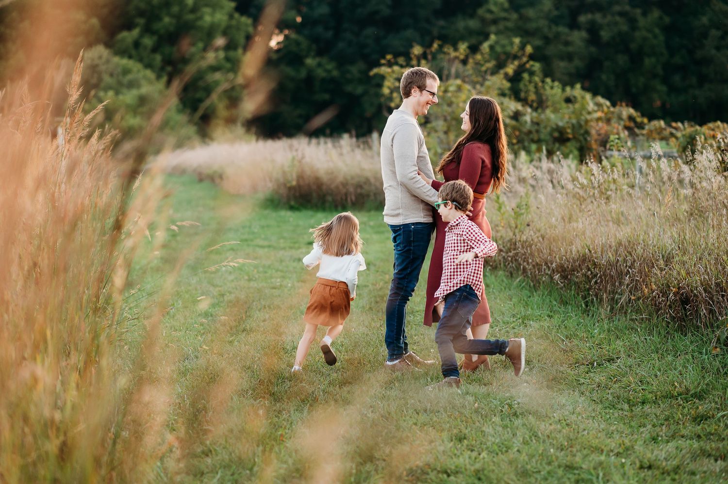 Family enjoying a playful moment together on a grassy path surrounded by tall autumn grasses and greenery.