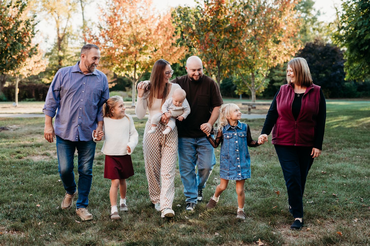 A family walks together with grandparents on an autumn day with colorful fall foliage in the background during a family photo session.