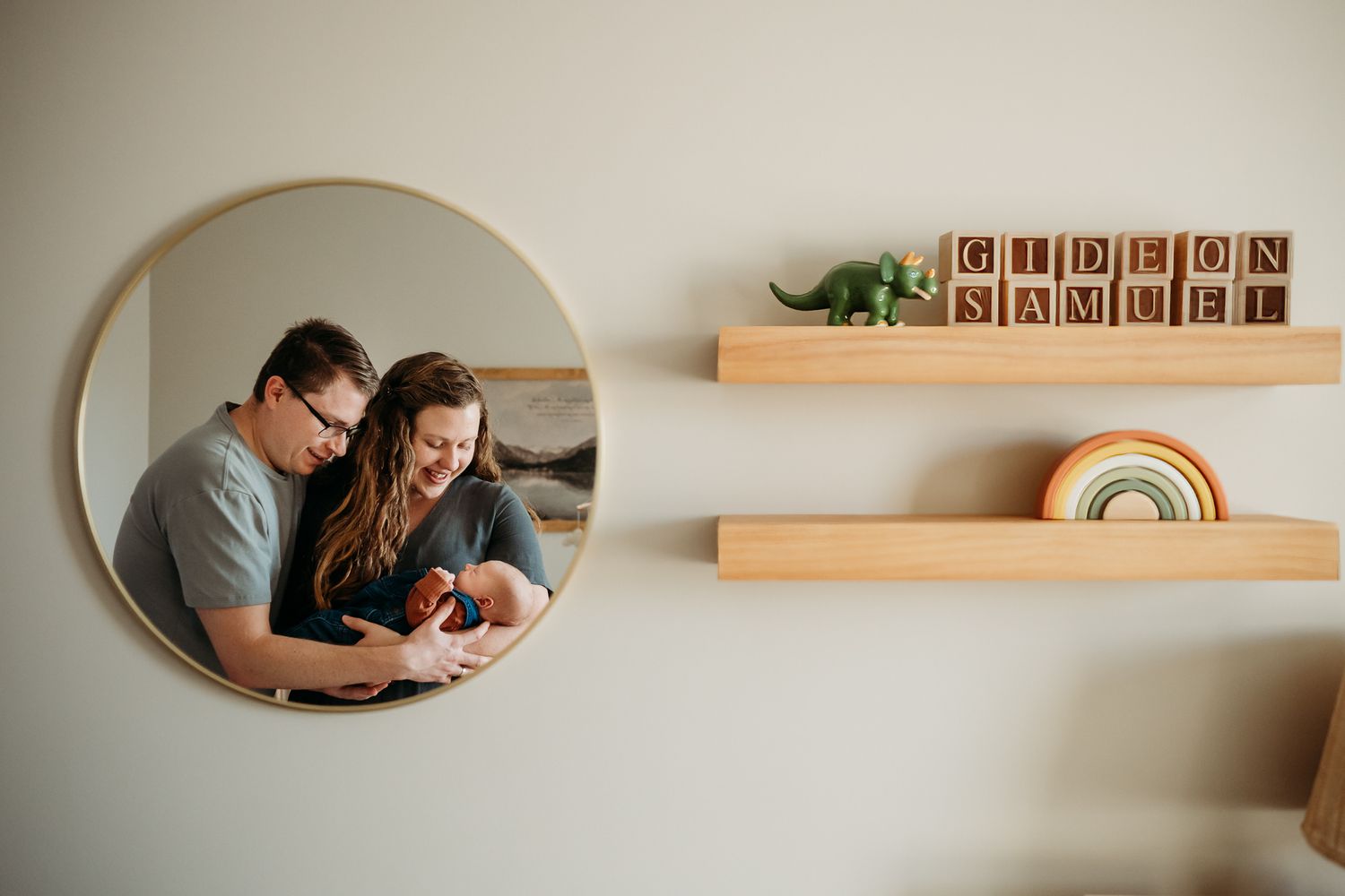A round mirror reflection shows a Greenwood, Indiana, couple looking down at newborn boy, with wooden shelves and decor in the background.