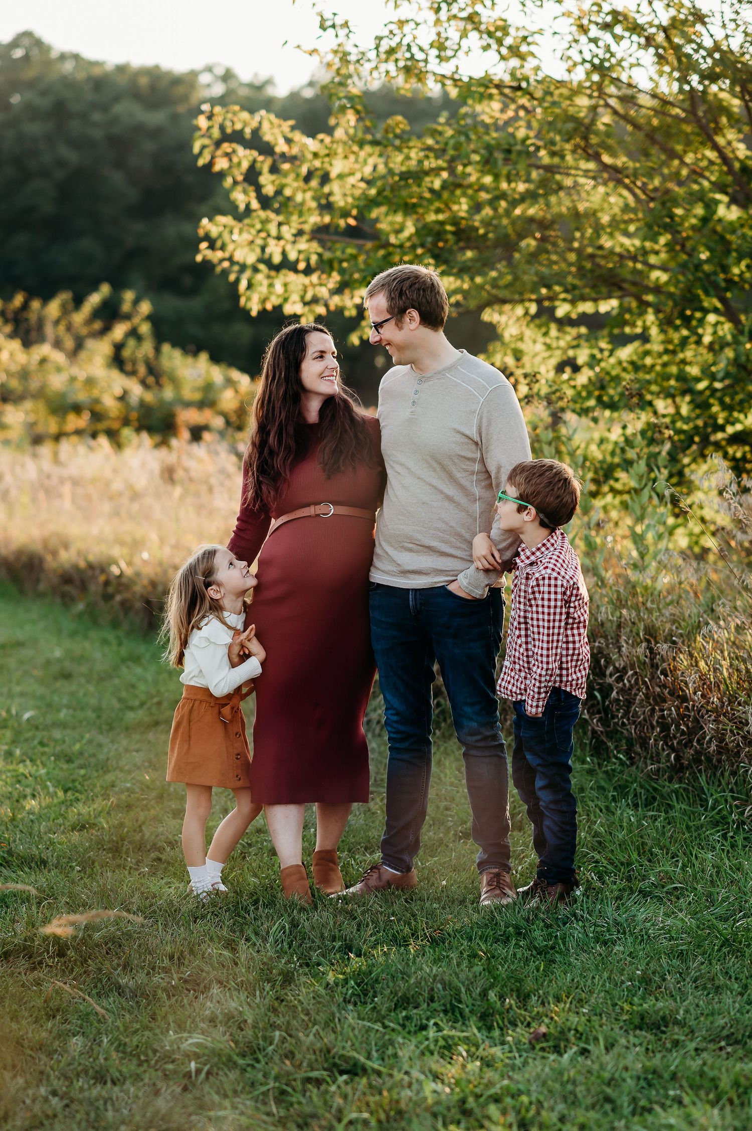 Family enjoying a golden sunset moment together in a grassy field during an outdoor maternity photo session in West Lafayette, Indiana.