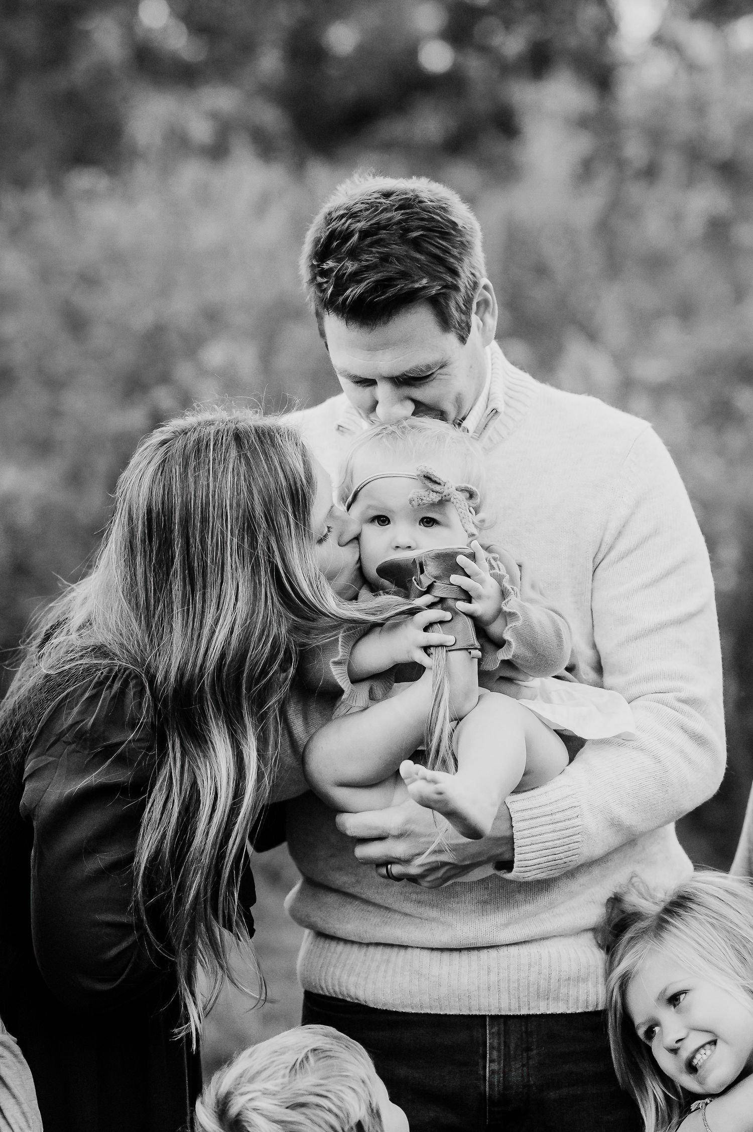 Black and white family moment showing parents and child sharing tender embraces outdoors during Family Photos at Ritchey Woods in Fishers IN
