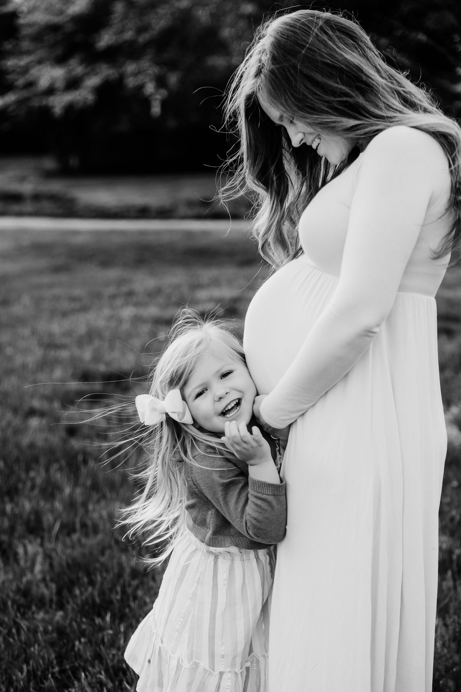 Black and white portrait capturing playful interaction between mom and daughter during spring maternity photos at Friendship Gardens.