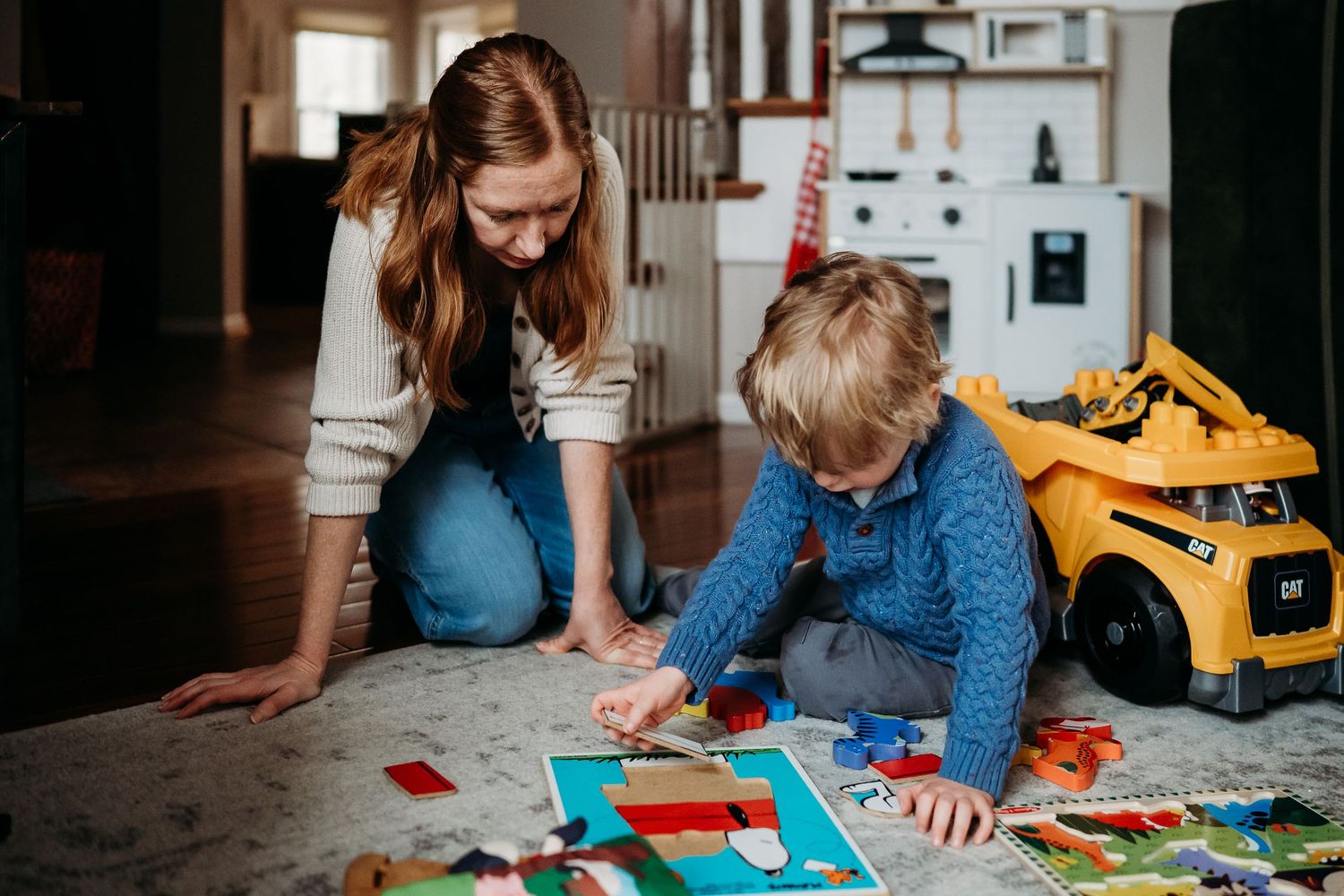 Woman and young boy playing with colorful puzzle toys together on living room floor at home.