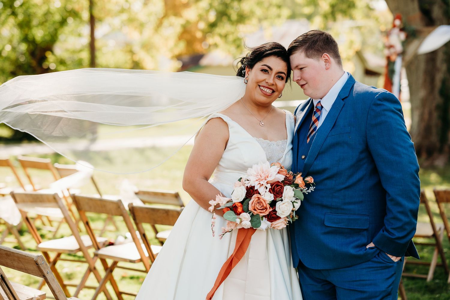 Couple in wedding attire share romantic moments in a garden setting with wooden chairs and natural sunlight.