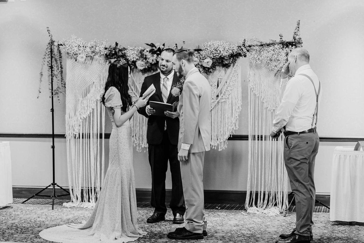 Wedding ceremony in progress with elegant white draping and decor in an indoor venue.