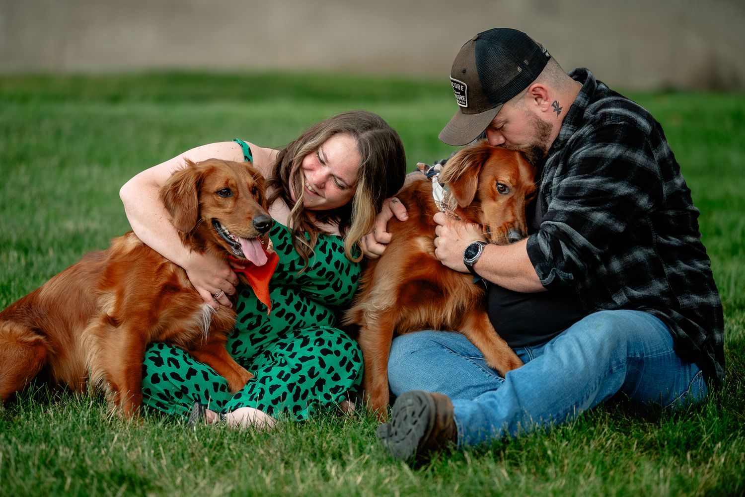 Couple sits on green grass cuddling two golden retrievers during golden hour dog photo session with Sara House Photography.