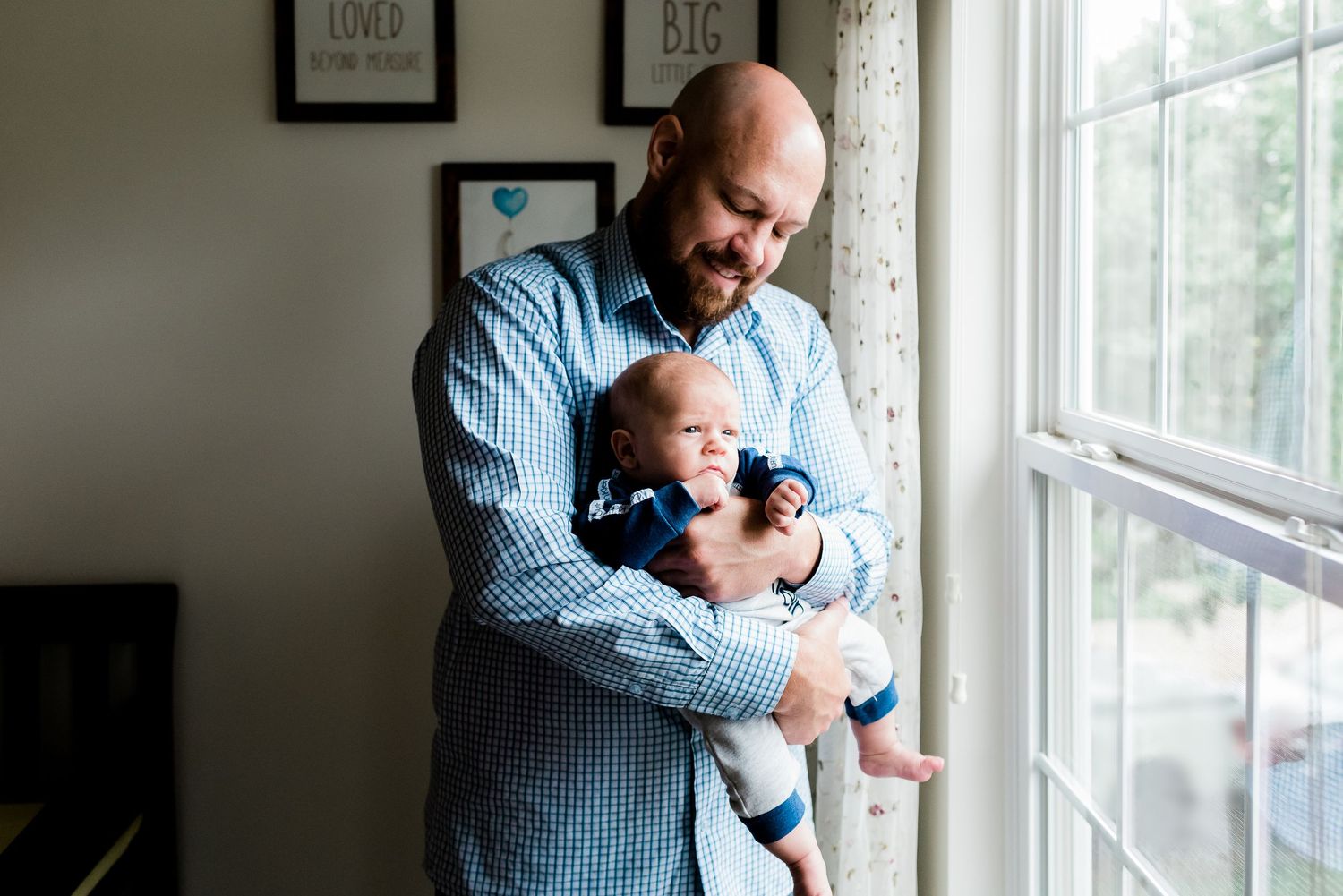 Tender dad and baby boy moment by a sunny window in cozy Avon, Indiana, home during lifestyle newborn photoshoot.