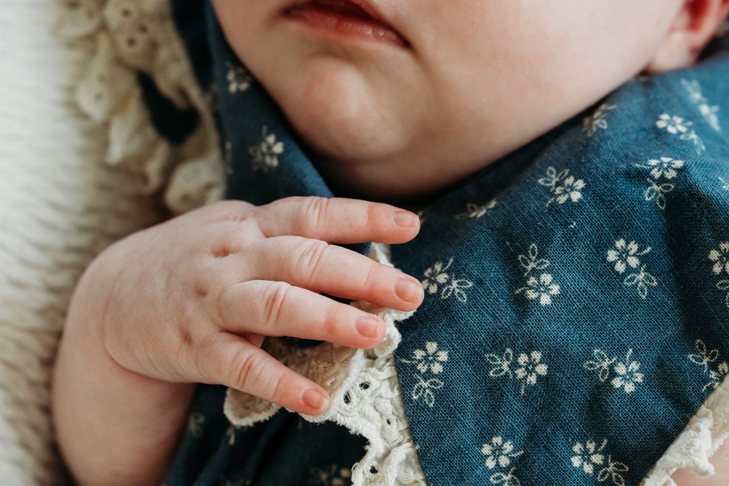 Close-up of a baby wearing a teal floral bandana bib, with tiny fingers grasping the fabric.
