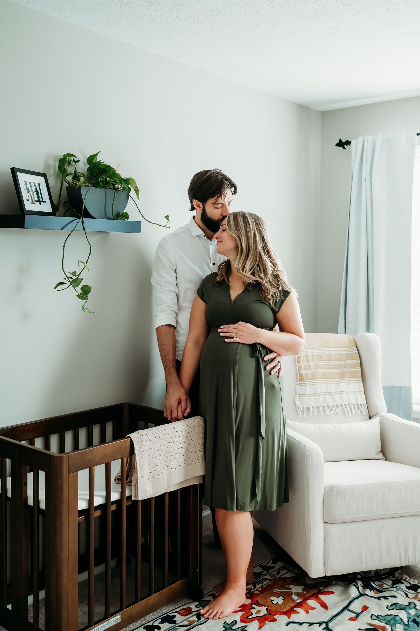 A couple sharing an intimate moment near a baby crib in a cozy nursery with indoor plants and floral rug.