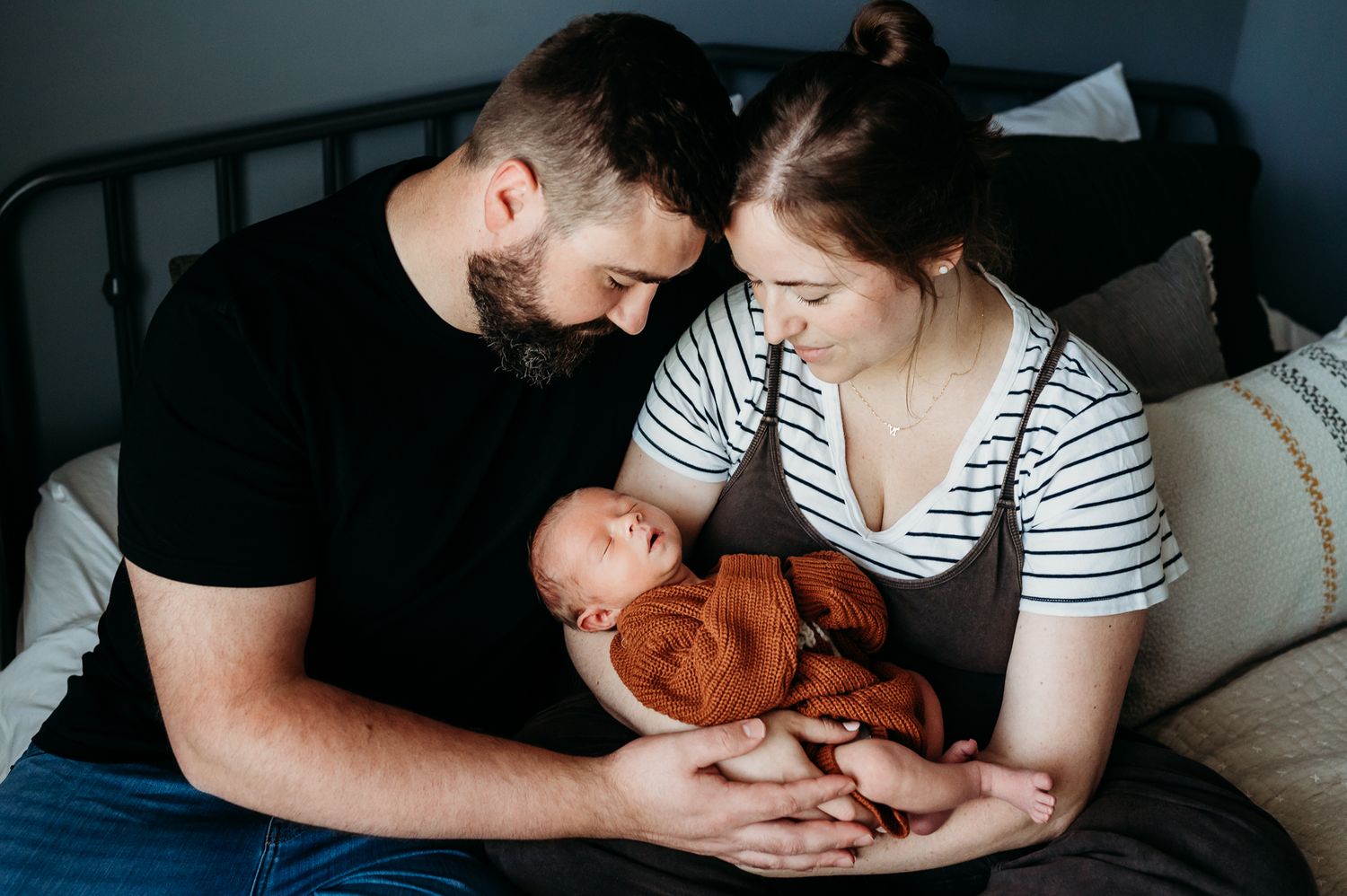 A tender family moment shows parents holding their newborn baby in a dimly lit room, captured in their Indiana home.