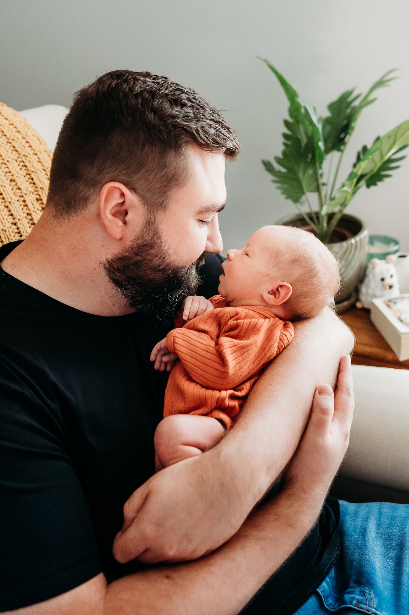 Dad rocking a baby wearing an orange onesie  during in-home Indiana newborn photo session with Sara House Photography.