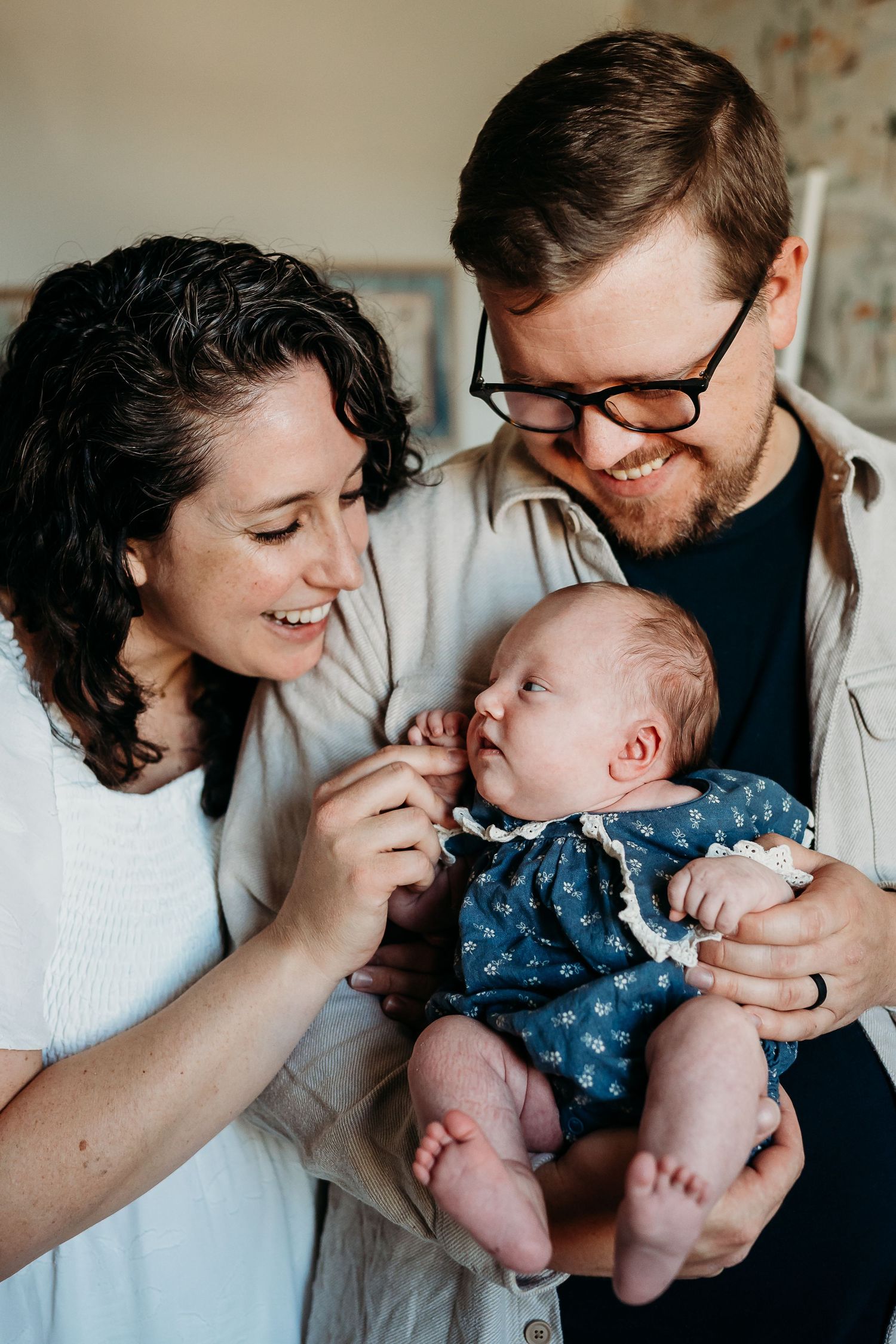 Smiling parents lovingly gaze at their newborn baby dressed in a blue floral outfit.