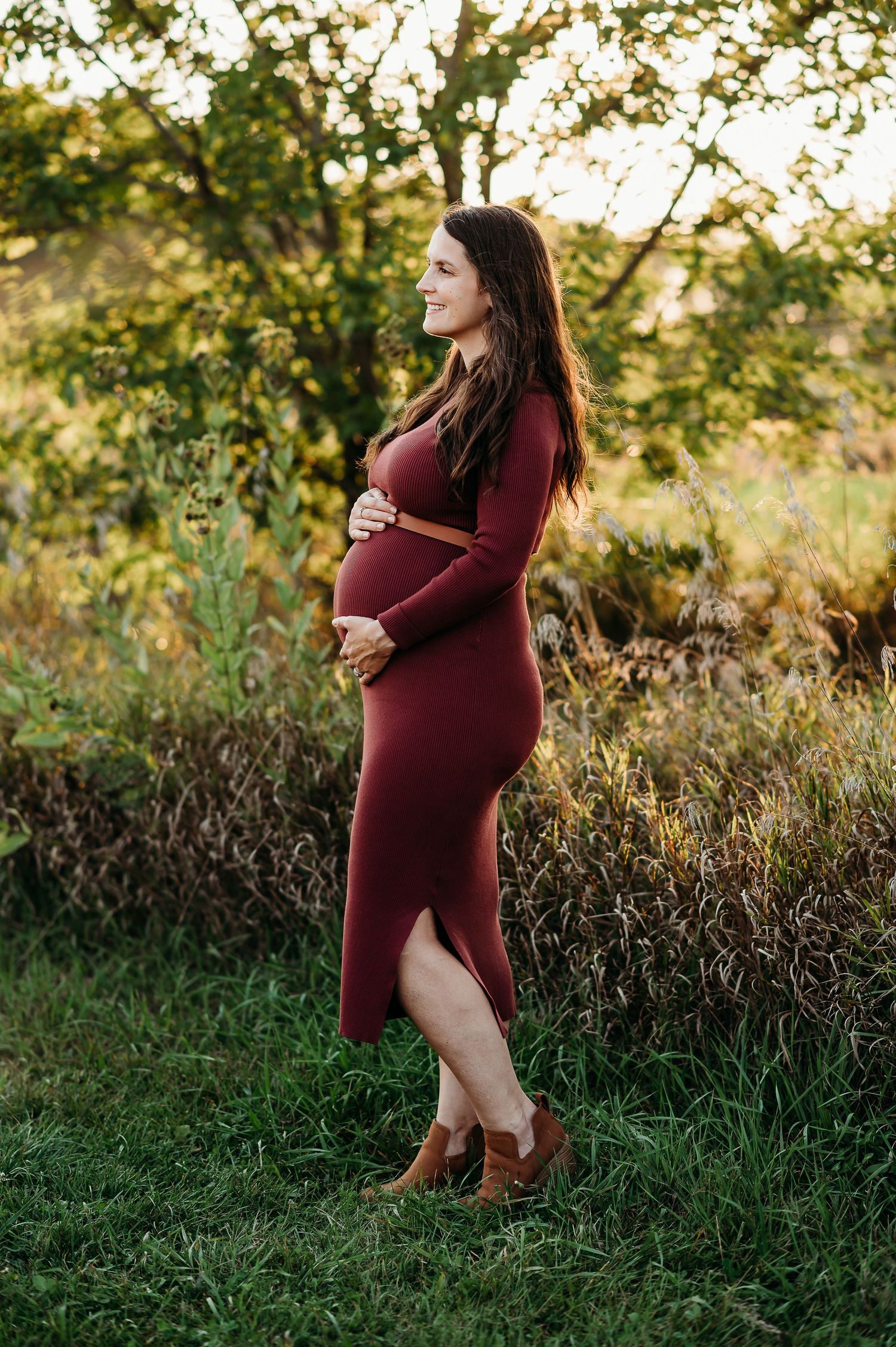 Maternity photo session in a natural setting with warm sunlight filtering through autumn trees.