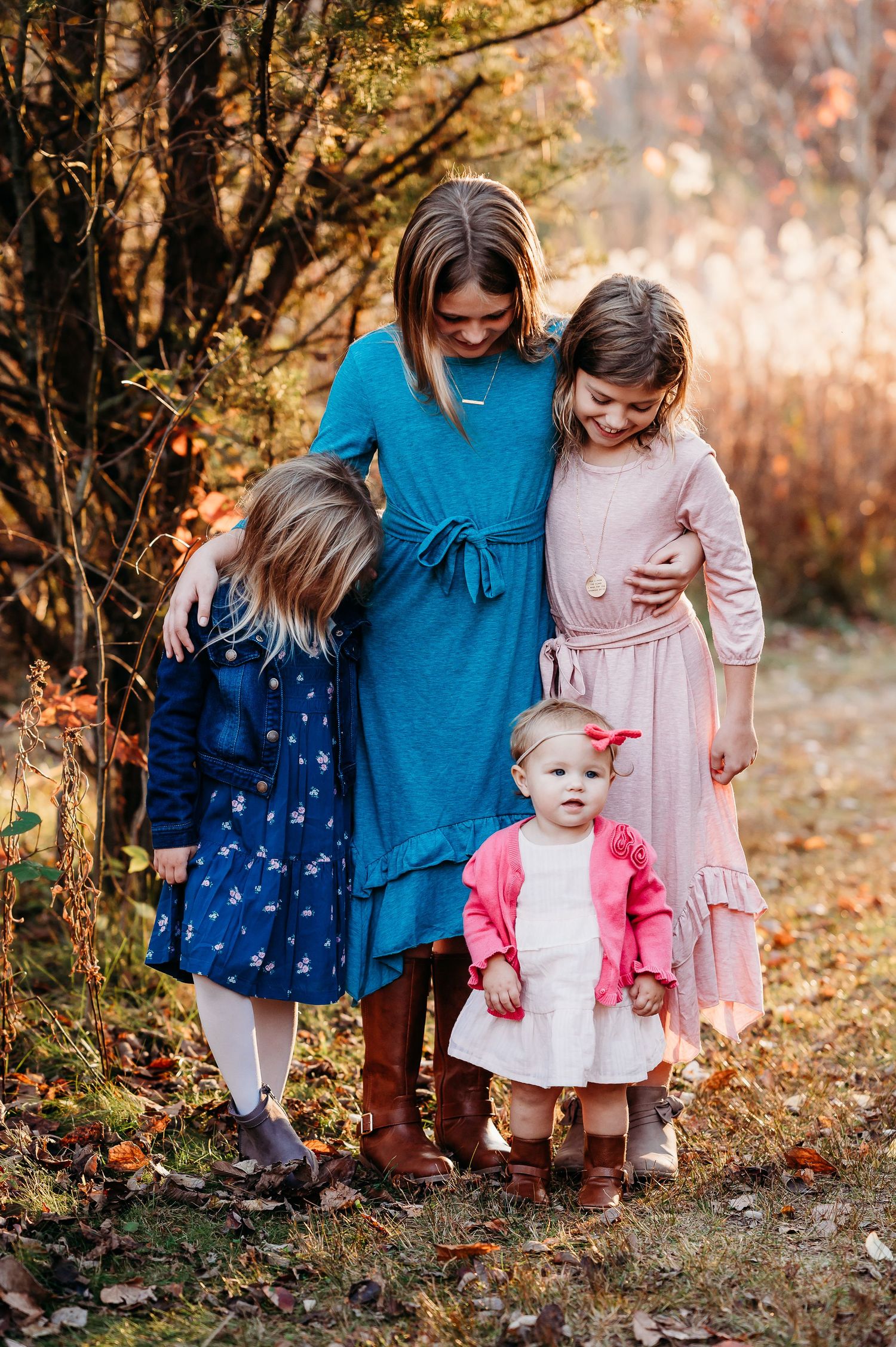 Sisters in blue and pink dresses stand together on autumn leaves at Fall Family Photoshoot at Ritchey Woods Nature Preserve in Fishers, IN.