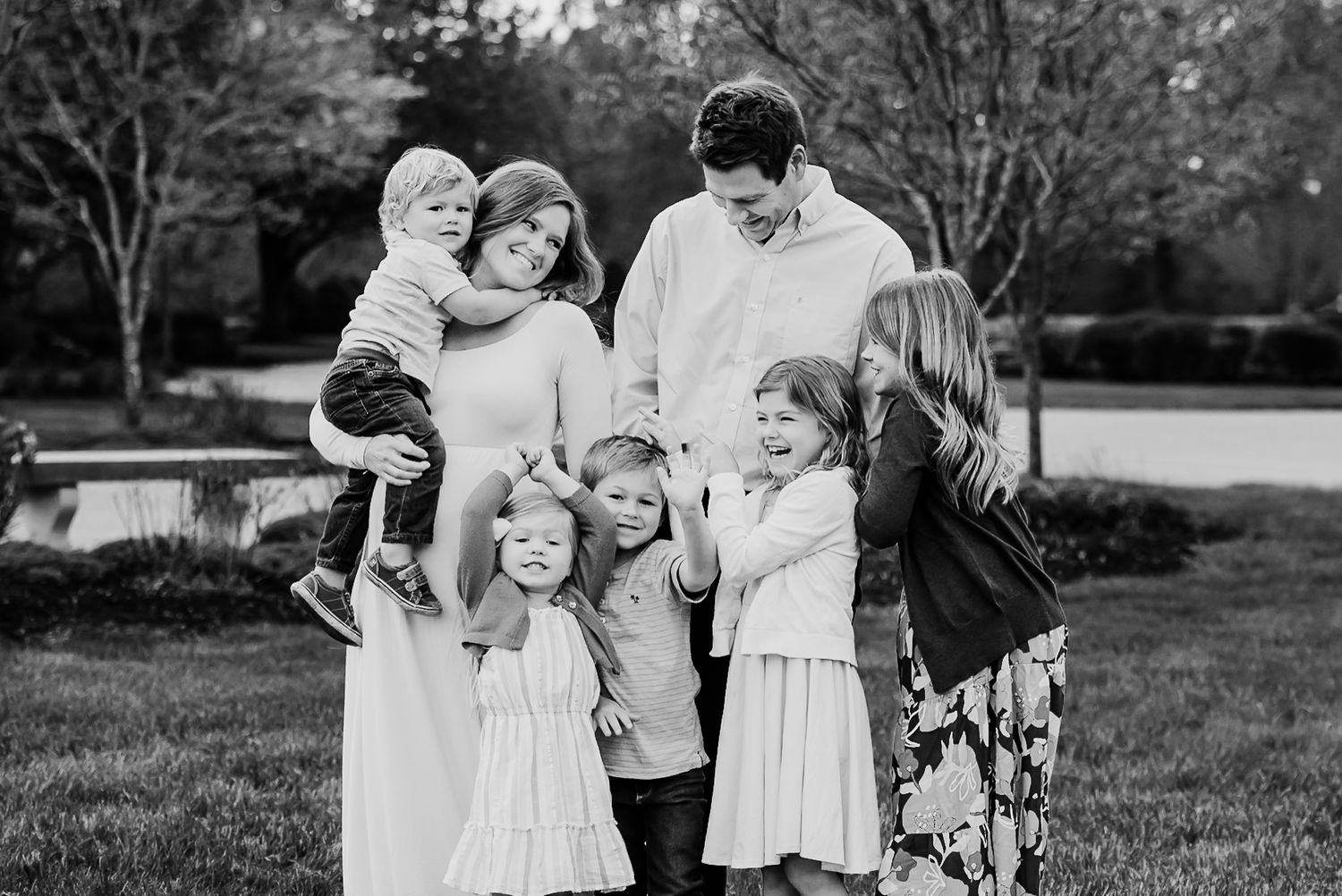 A candid black and white outdoor family portrait showing a group of people embracing and laughing together in a garden setting.