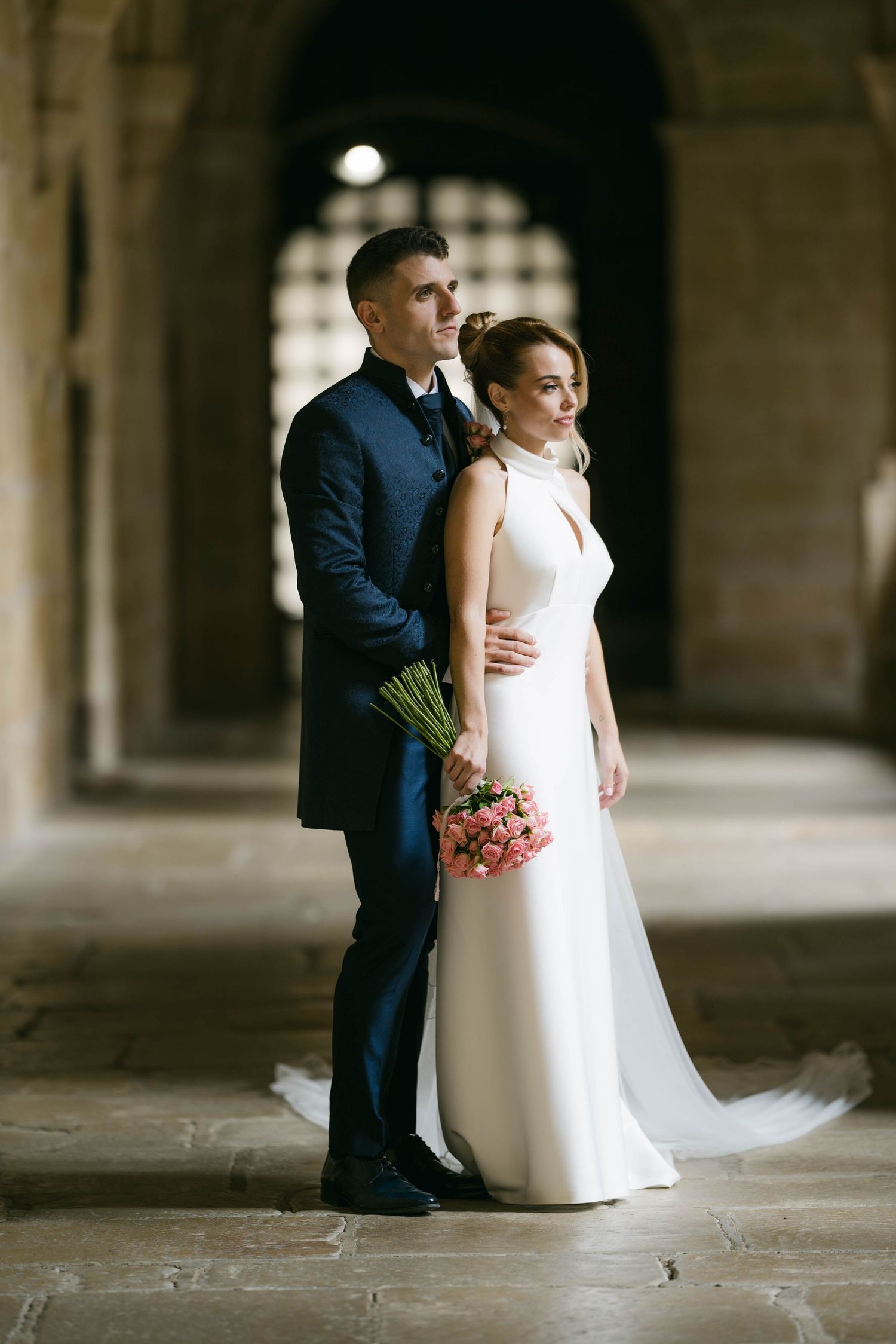 A couple in wedding attire poses together in a series of romantic shots under an elegant stone archway.