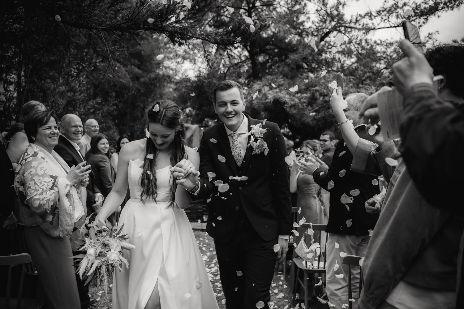 Wedding celebration with guests throwing confetti during outdoor ceremony exit.
